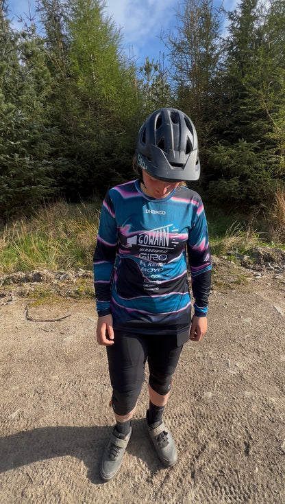 Person wearing the colorful Gowaan Racing Dharco cycling jersey and helmet on a dirt path with trees in the background